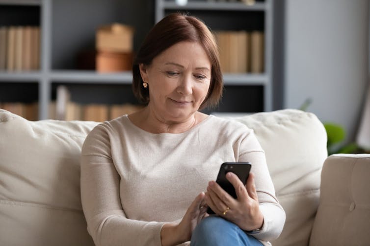 Middle-aged woman sitting on sofa scrolling smartphone