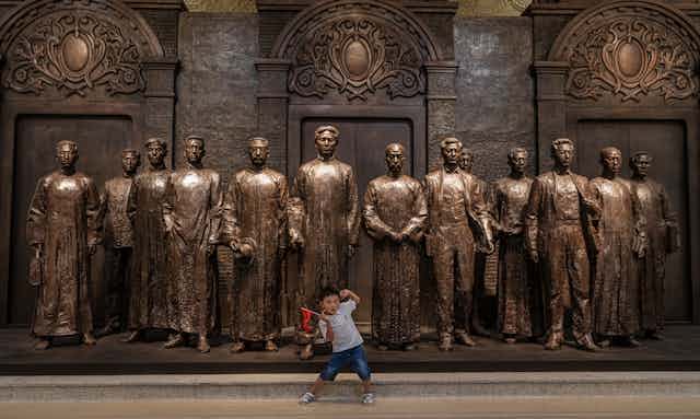A young boy poses in front of 13 statues depicting the founders of the Chinese Communist Party in Shanghai, 1921.