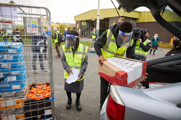 Marcus Rashford and his mother wear hi-vis vests and COVID face shields while loading food into cars at a food bank