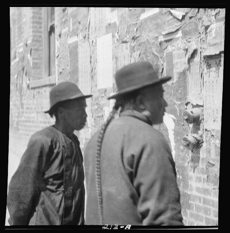 An archive photo depicting two men reading a notice in Chinatown