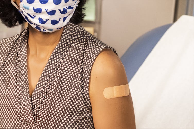 Woman in mask with a bandaid on her arm, after being vaccinated.
