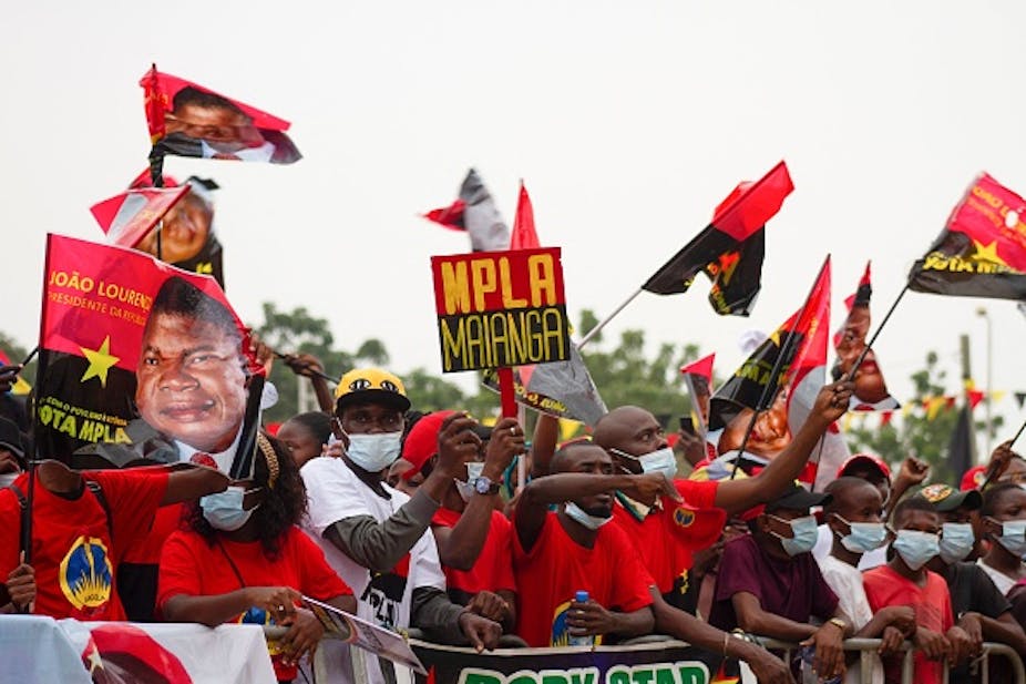 People wearing COVID-19 masks wave Angolan flags and those bearing the face of President João Lourenço.