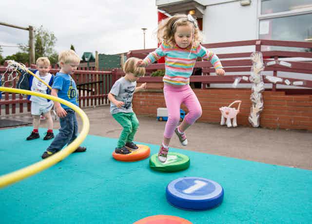 Four pre-school children jump on coloured cushions in a playground