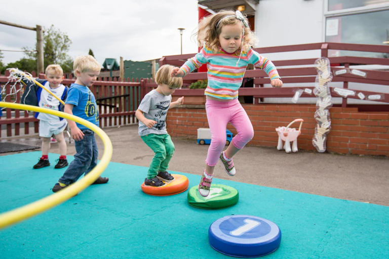 Four pre-school children jump on coloured cushions in a playground