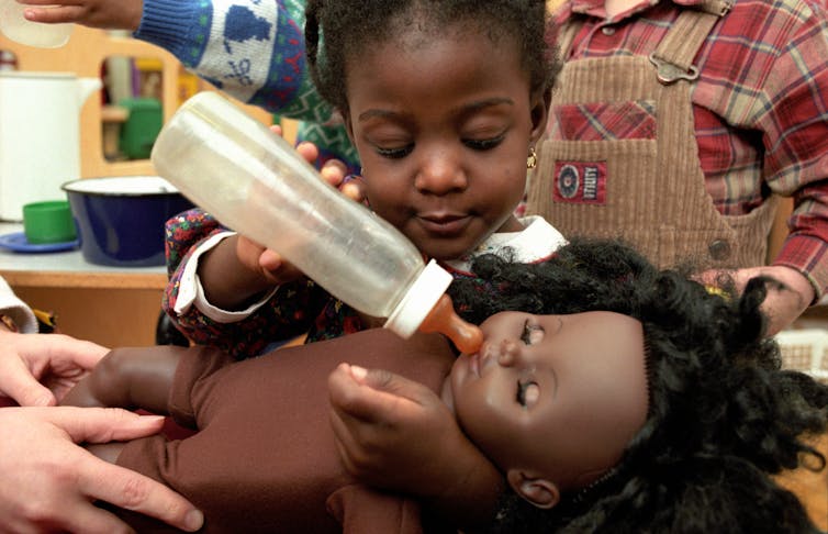 A little girl plays with a doll and a baby bottle