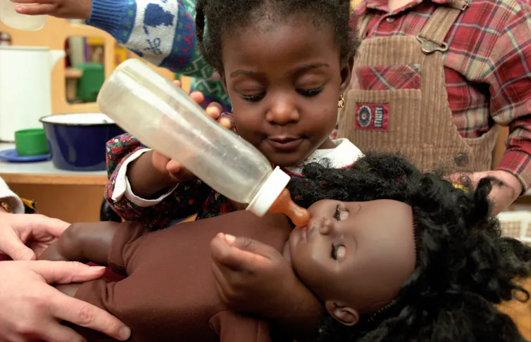 A little girl plays with a doll and a baby bottle