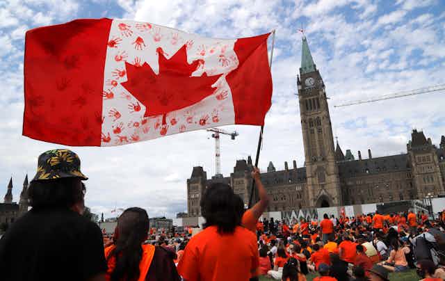 Protesters wave a Canadian flag imprinted with the hand prints of children in red.