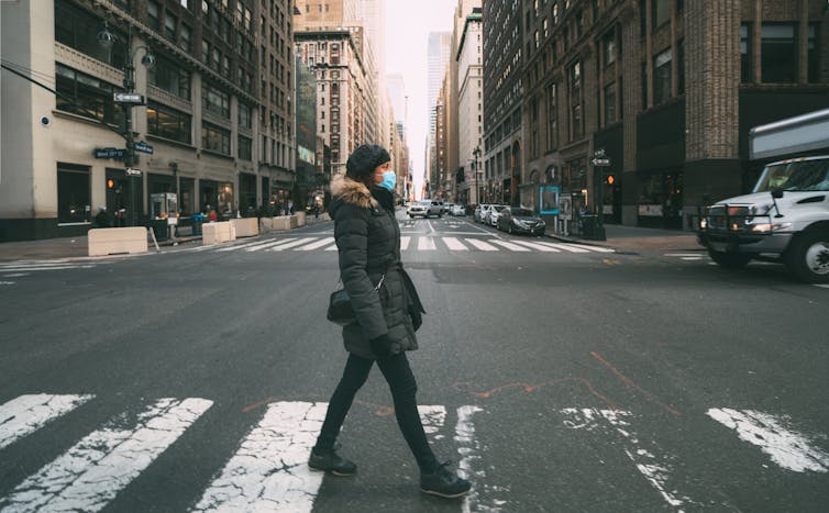 A woman wearing a mask crosses the street in New York.