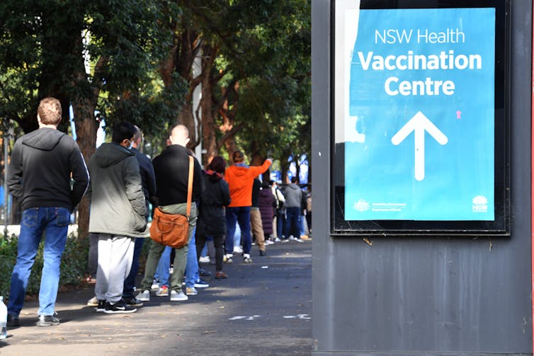A queue of people lining up, with a sign 'NSW Health Vaccination Centre'.