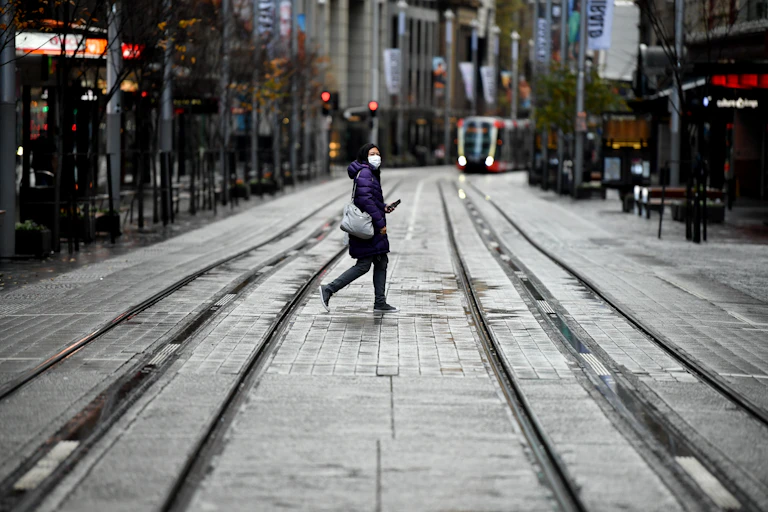 Person wearing mask walking across road with tram in background