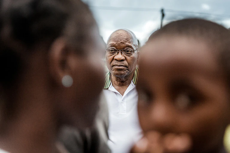 Woman and child out of focus in the foreground, elderly man's face in focus in the background