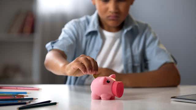 Boy putting coin in piggy bank.