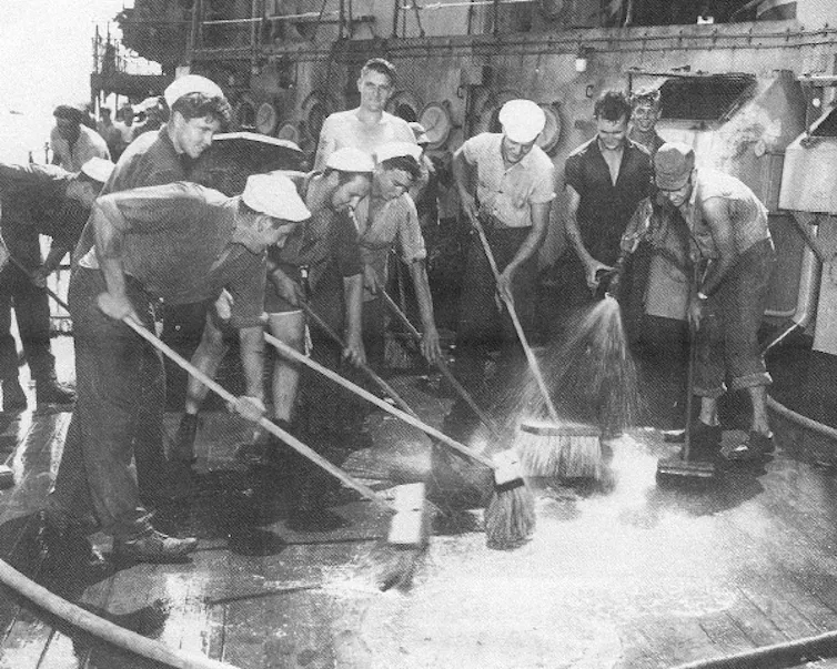 A group of men brushing and cleaning the deck of a ship to try to remove the radiation fallout from an atomic explosion.