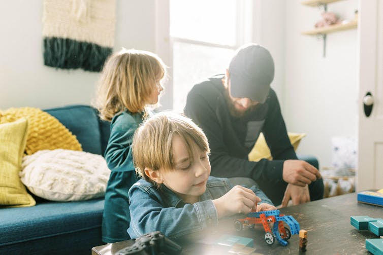 A little boy plays at a table at home with his sister and father nearby