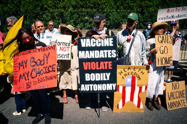 Anti-vaxxers hold signs reading 'my body my choice' 'vaccine mandates violate bodily autonomy'