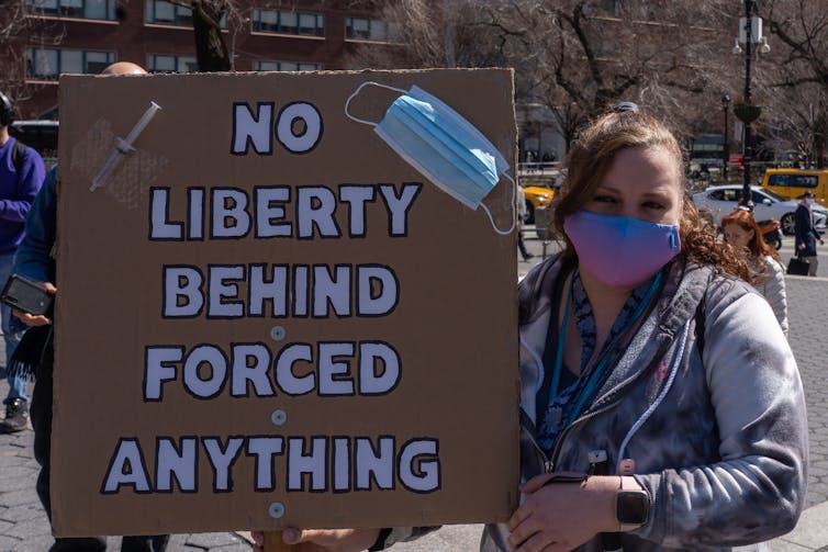 A woman stands holding a sign that reads 'no liberty behind forced anything'