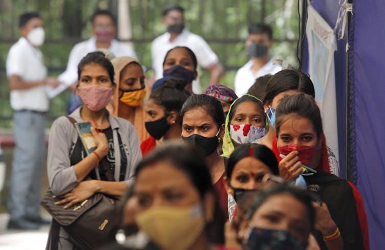 A group of women wearing masks line up to get vaccinated against COVID-19.