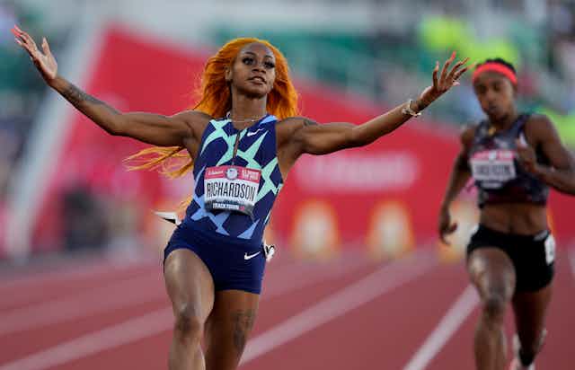 Richardson stretches both arms and lifts her hands after crossing the finish line