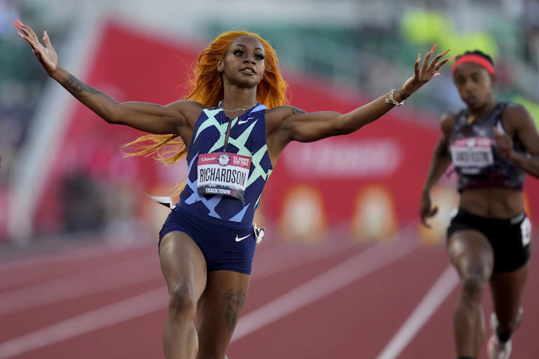 Richardson stretches both arms and lifts her hands after crossing the finish line