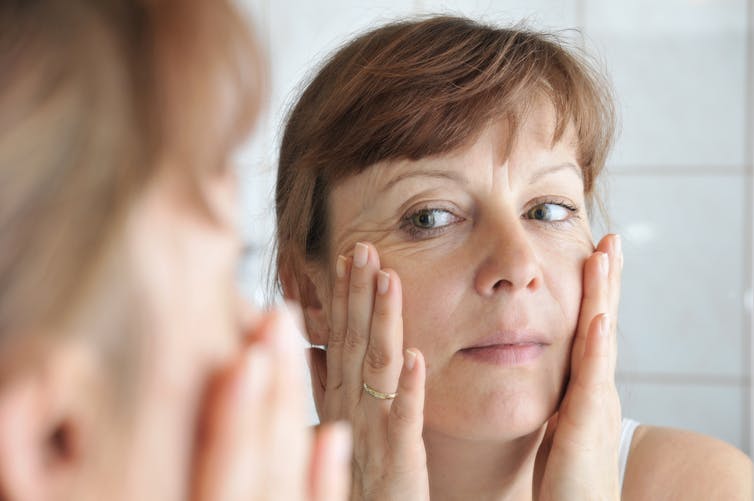 Woman in her 40s looks in the mirror and stretches her wrinkled skin.