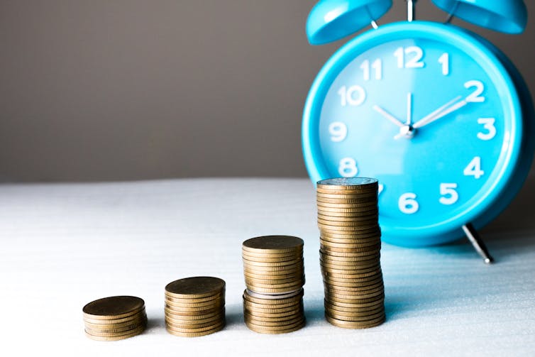 Four stacks of coins of various heights in front of a clock.