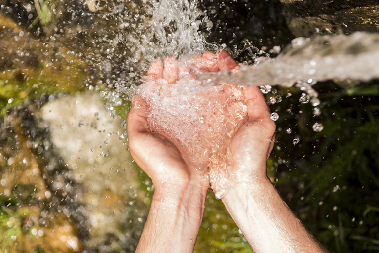 Chorro de agua cayendo sobre manos en cuenco.