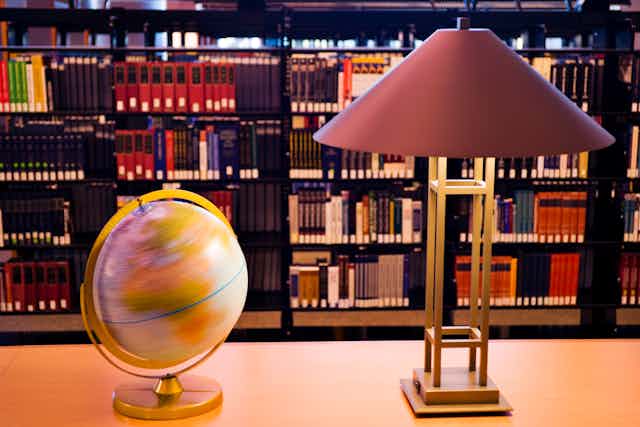 Globe and lamp on a table, with shelves of books in the background