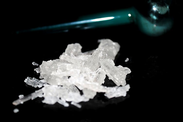 White methamphetamine crystals on a black background with a glass meth pipe.