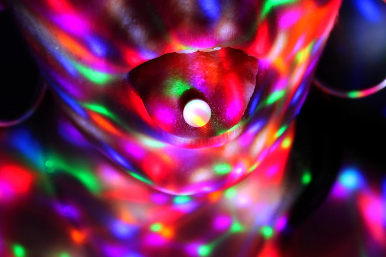 Una persona con una pastilla en la lengua alumbrada por luces de discoteca.