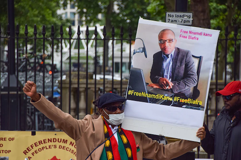 A man wearing a mask, raising his fist and holding up a placard with his other hand.