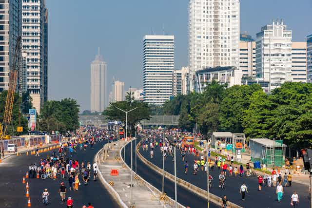 Crowds of pedestrians walk down an empty dual carriageway in central Jakarta