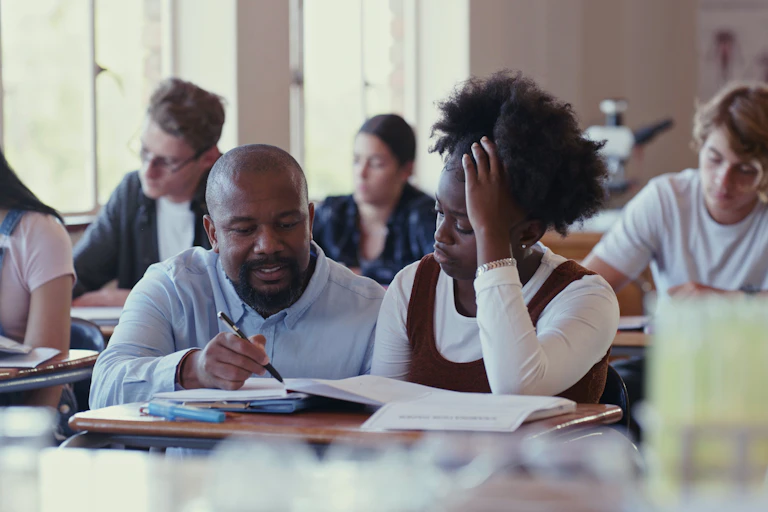 A teacher assisting a student with schoolwork in a classroom.