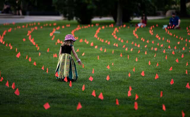 Little girl stands amid flags representing children who died at Indian Residential Schools