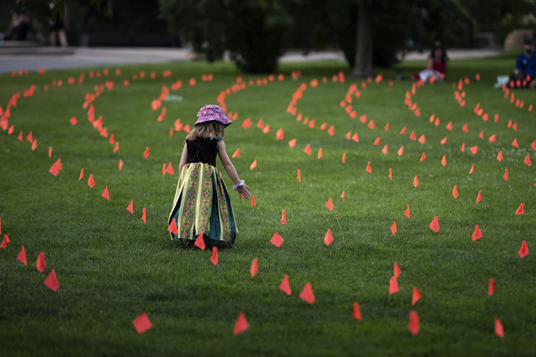 Little girl stands amid flags representing children who died at Indian Residential Schools