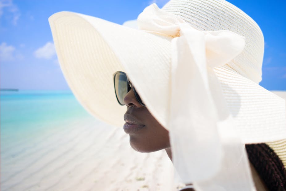 A portrait of woman wearing a summer hat and sunglasses on tropical beach.