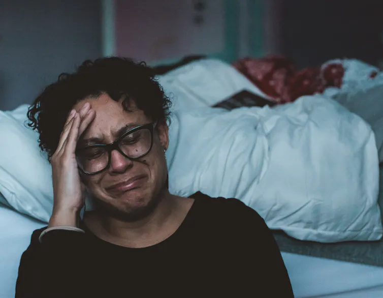 Woman sitting on the floor crying with her hand on her face