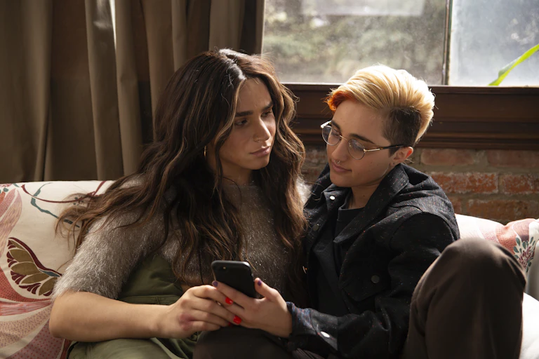 A transfeminine non binary person and transmasculine gender nonconforming person looking at a phone with upset expressions