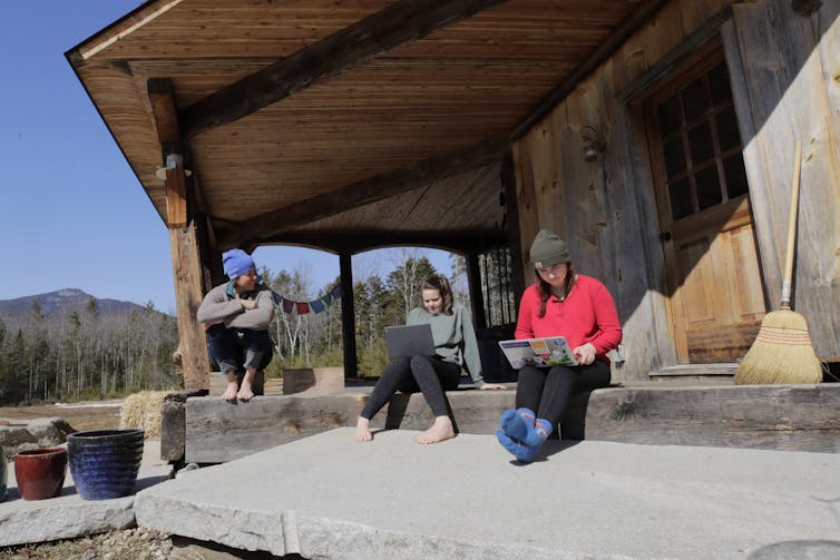 Three people sitting on a porch trying to connect their laptops to internet.