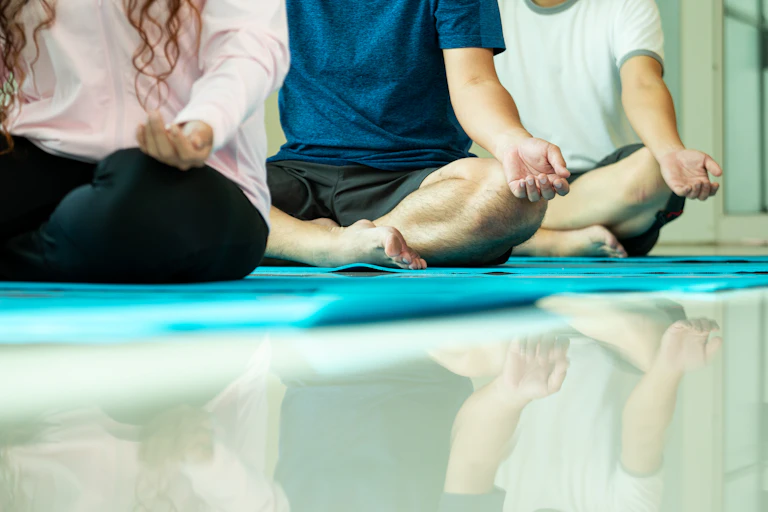 Three people sit on mats with their legs crossed in a meditation pose.