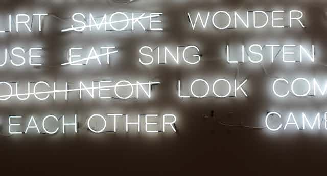 A neon sign of floating words, some of which say Please dance touch feel wonder