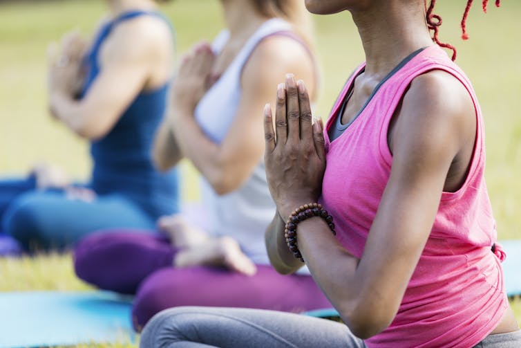 Three diverse women practicing yoga outdoors, with a Black woman in the focus