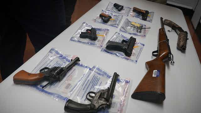 A collection of illegal guns including eight pistols and a rifle is displayed on a table during a gun buyback event in Brooklyn, New York.