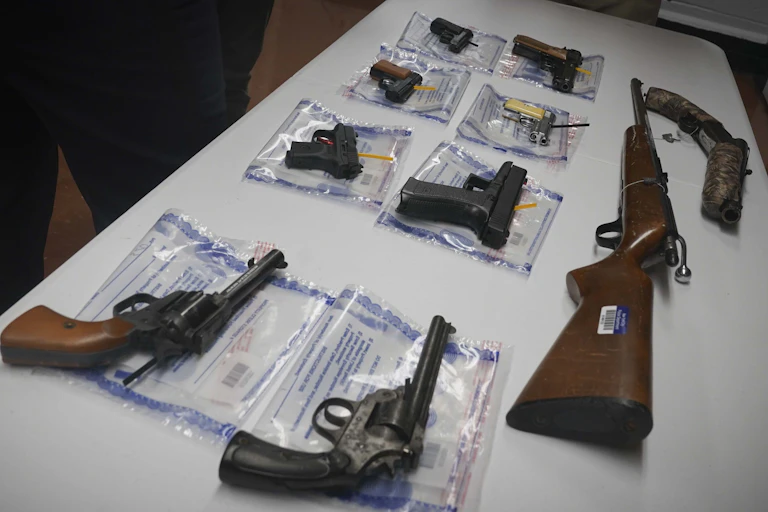 A collection of illegal guns including eight pistols and a rifle is displayed on a table during a gun buyback event in Brooklyn, New York.