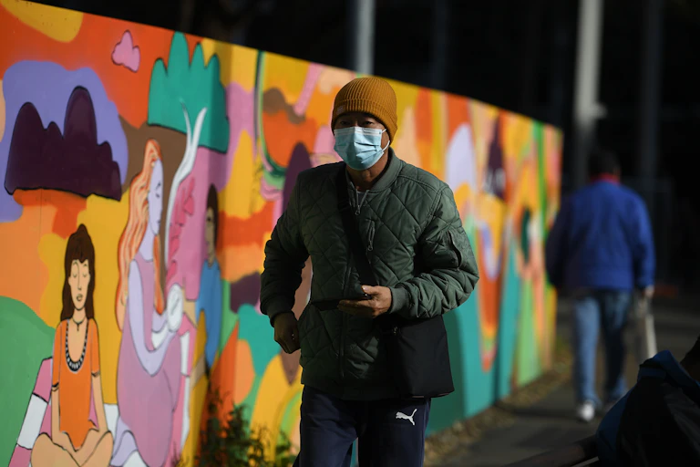Man in mask walks next to colourful mural.