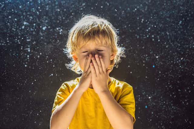 Un niño se echa las manos a la nariz para estornudar.
