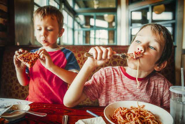 Dos niños comen pasta y pizza.