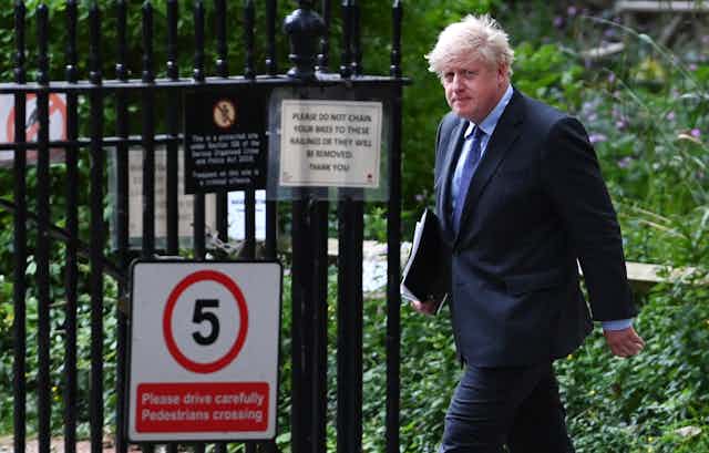 Prime minister Boris Johnson walks outside, carrying a folder of papers and looking solemn