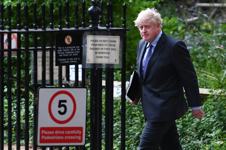 Prime minister Boris Johnson walks outside, carrying a folder of papers and looking solemn