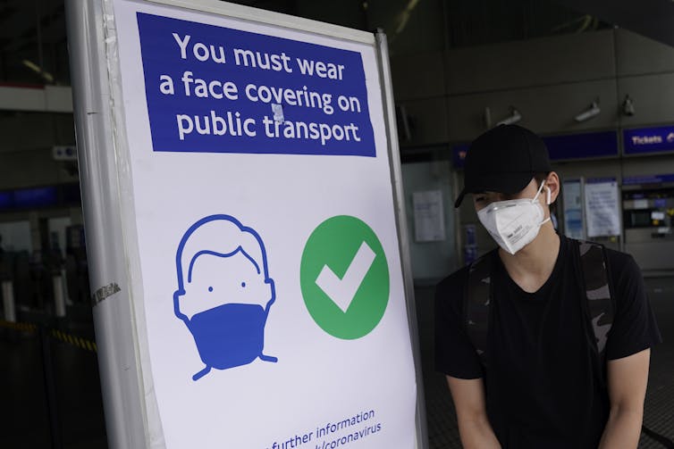 A commuter in a face mask walks by a sign that says