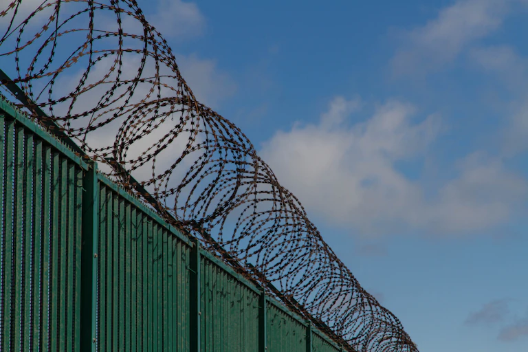 A high fance with a roll of razor wire along the top.